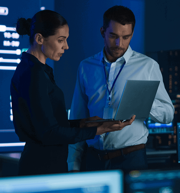 A man and woman inside a government data/control room looking at a laptop