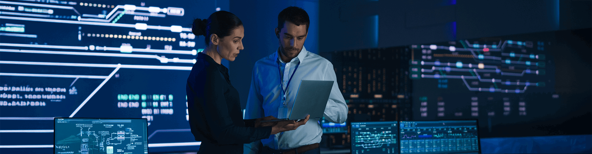 A man and woman inside a government data/control room looking at a laptop